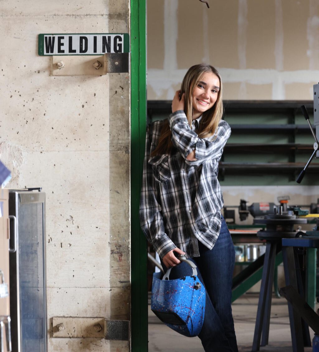 Student leaning against doorframe in the Hanna Academy welding shop.