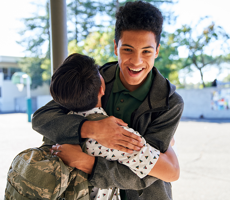 Student smiling while hugging a friend outdoors on campus.