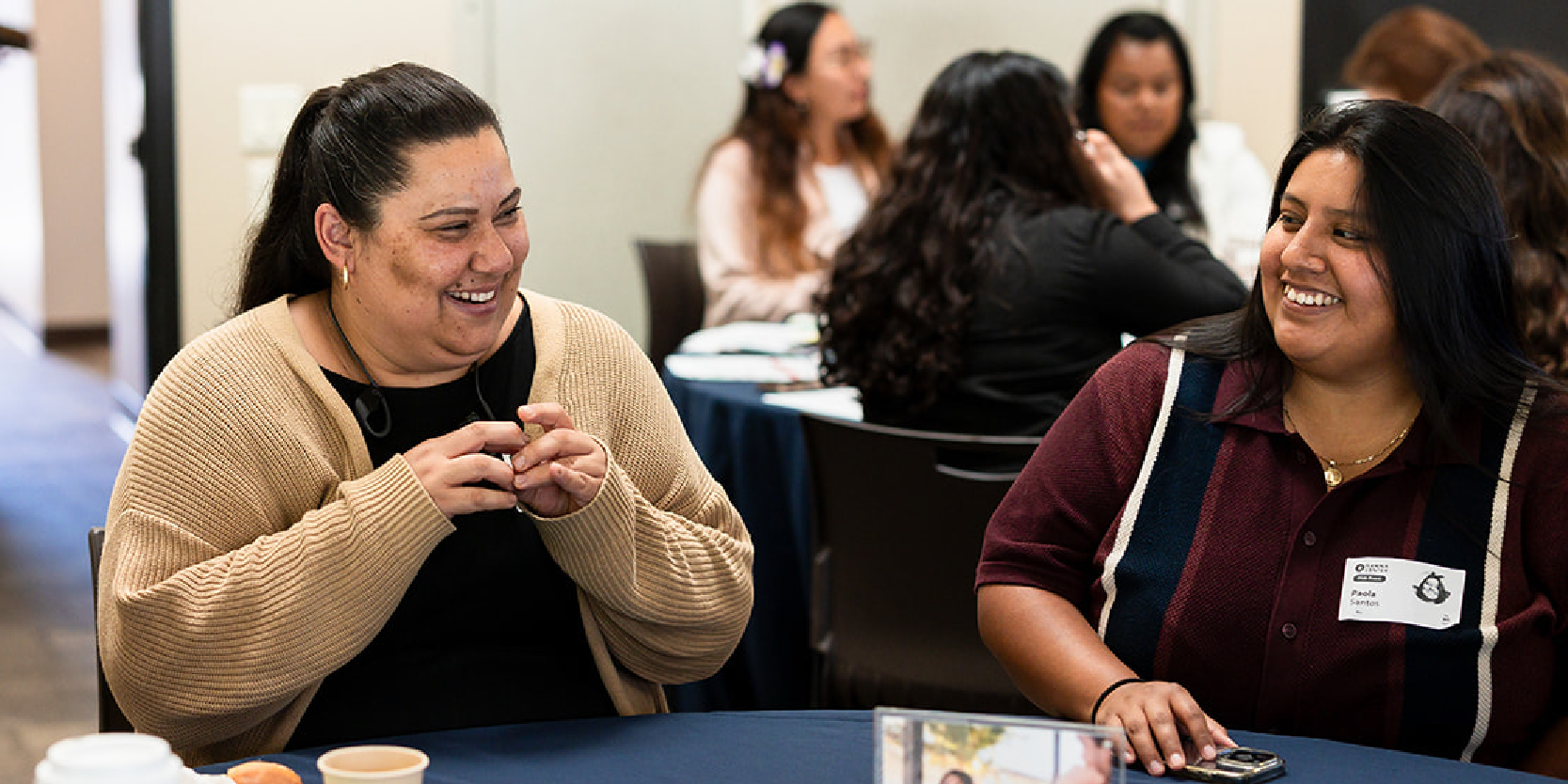 Two community members smiling and looking at each other while sitting at a table.