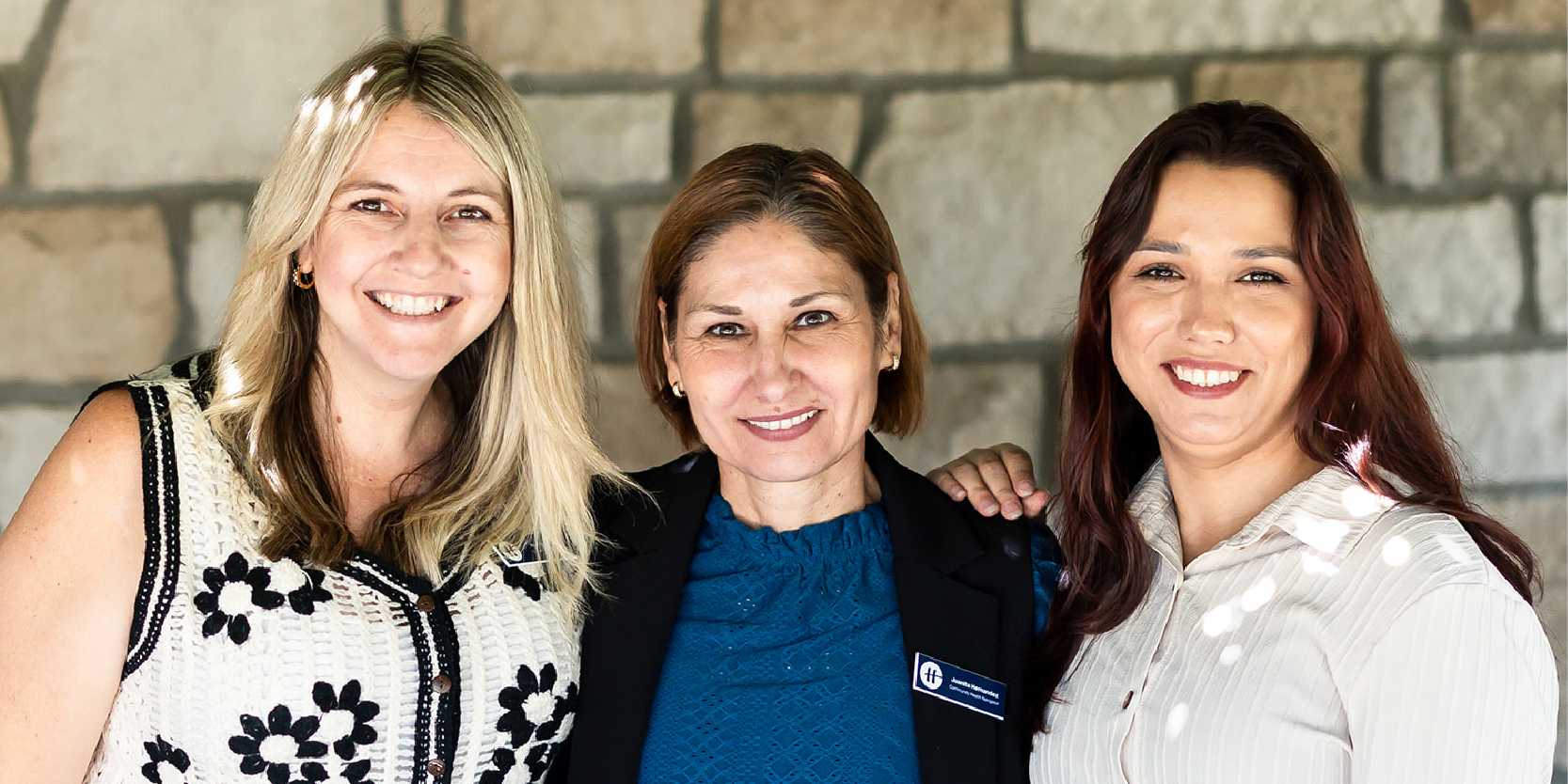 Three people smiling for a photo against a beige brick background.