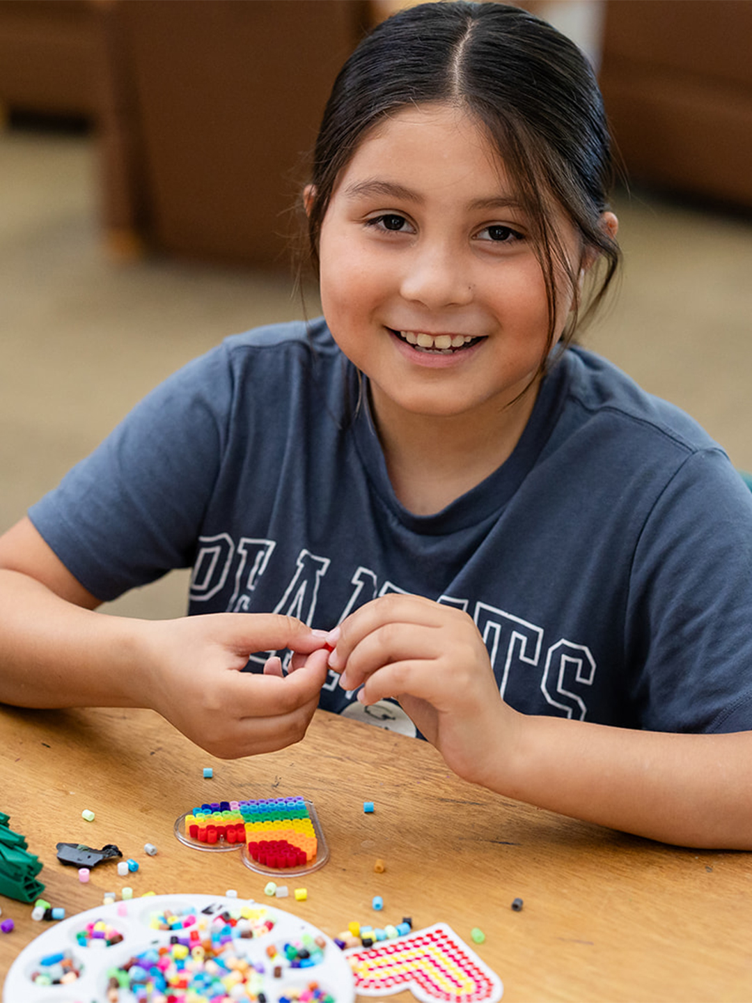 Smiling camper making colorful bead art at a table during Hanna Center camp.