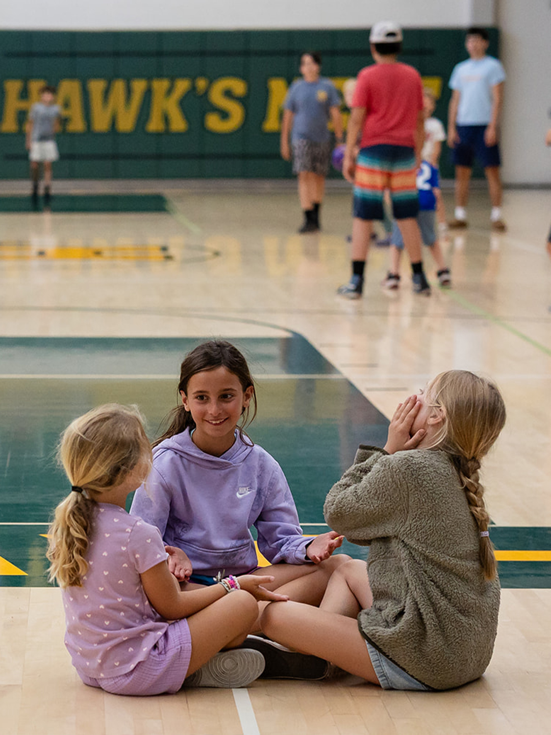 Three campers sit together and talk on the gym floor during Hanna Center camp.