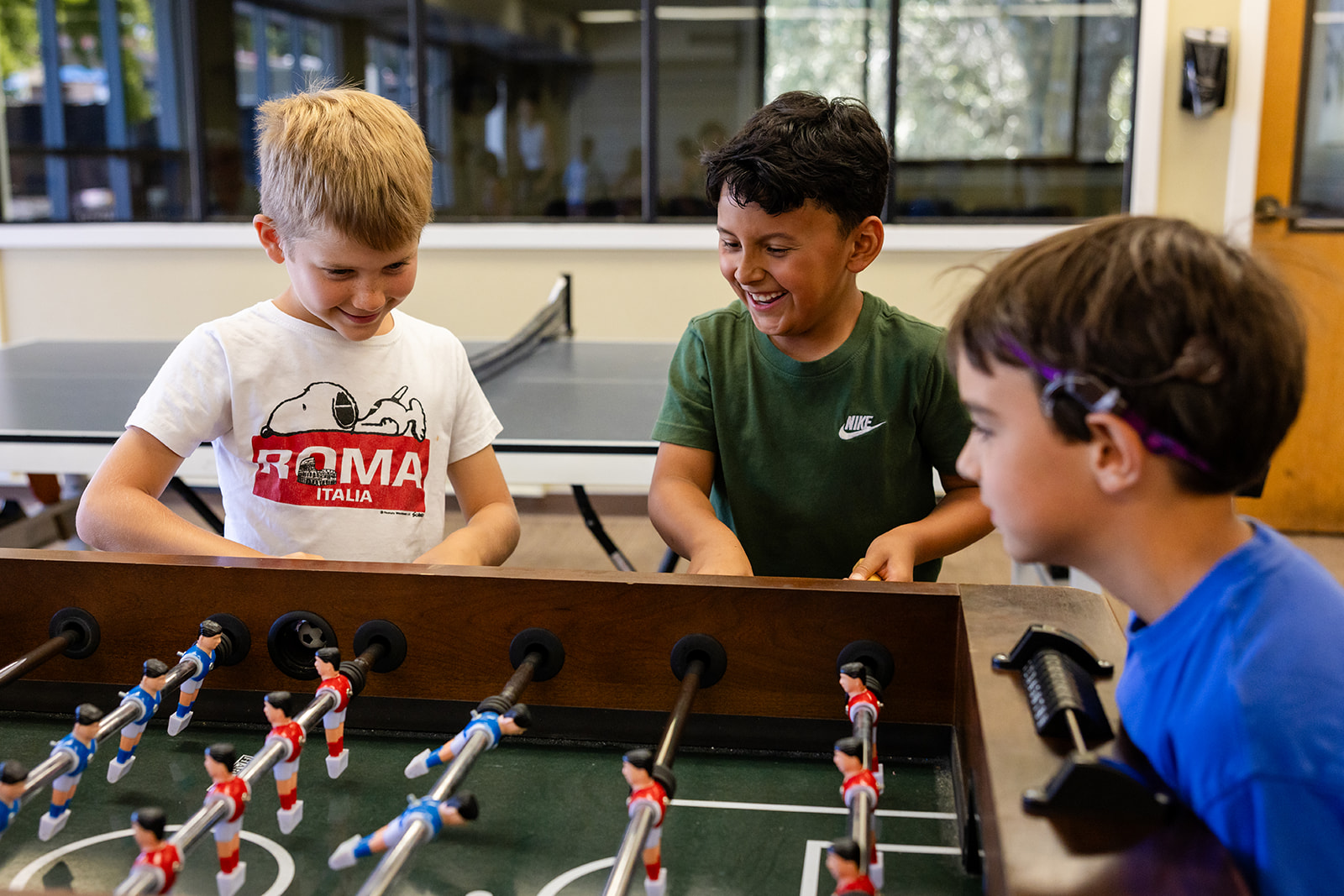 Three campers smiling while playing foosball in the Hanna Center Recreation Center.