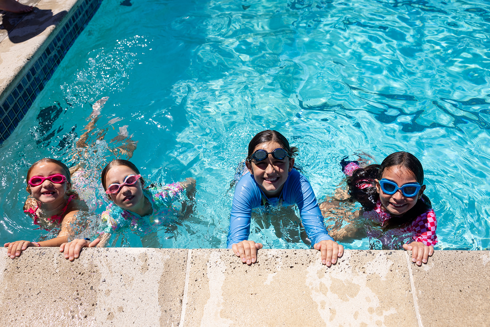 Four campers wearing goggles smile at the edge of a swimming pool during Hanna Center camp.
